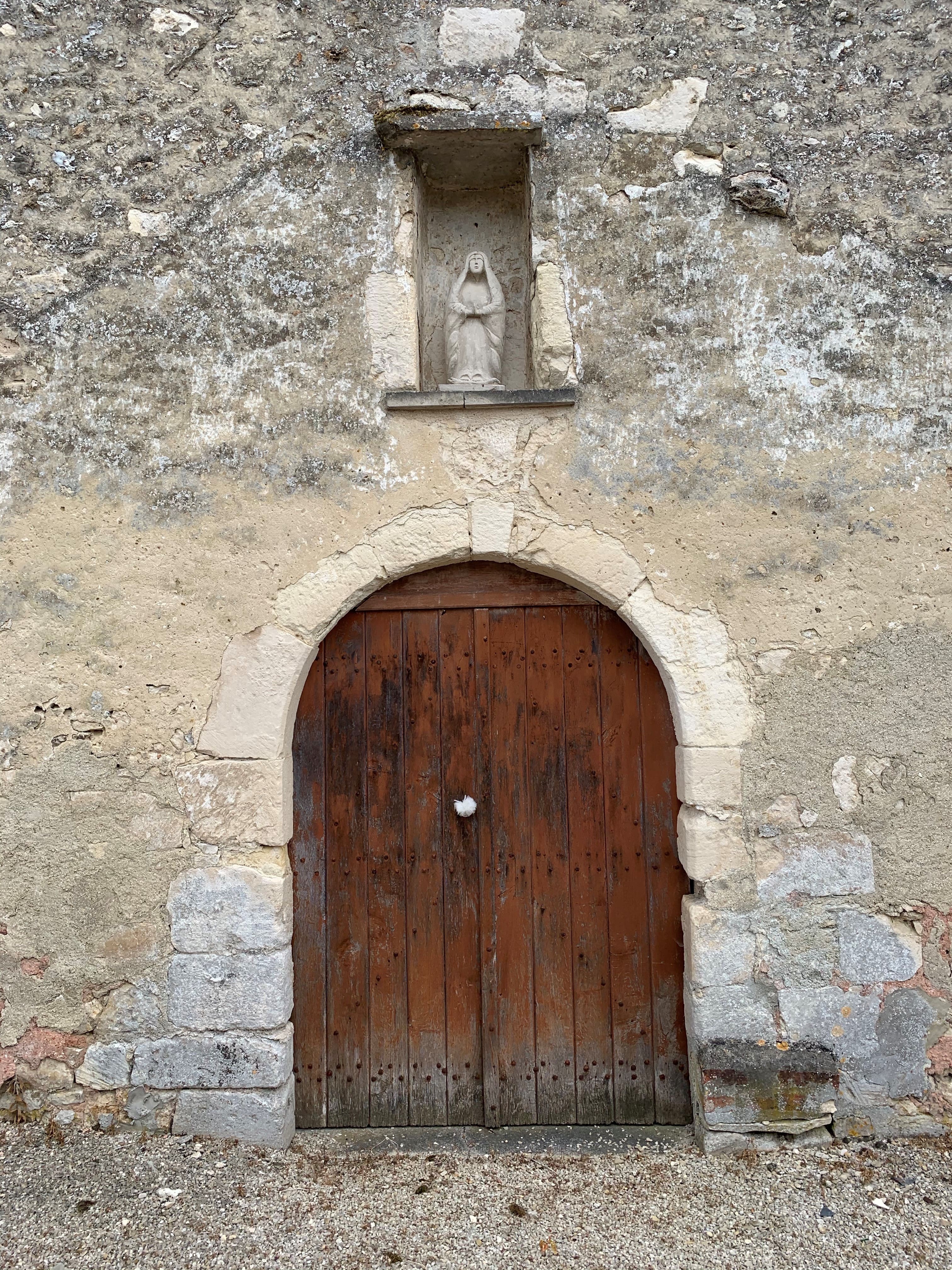 Façade de l'église avec porte voûtée, niche et statue de la Vierge