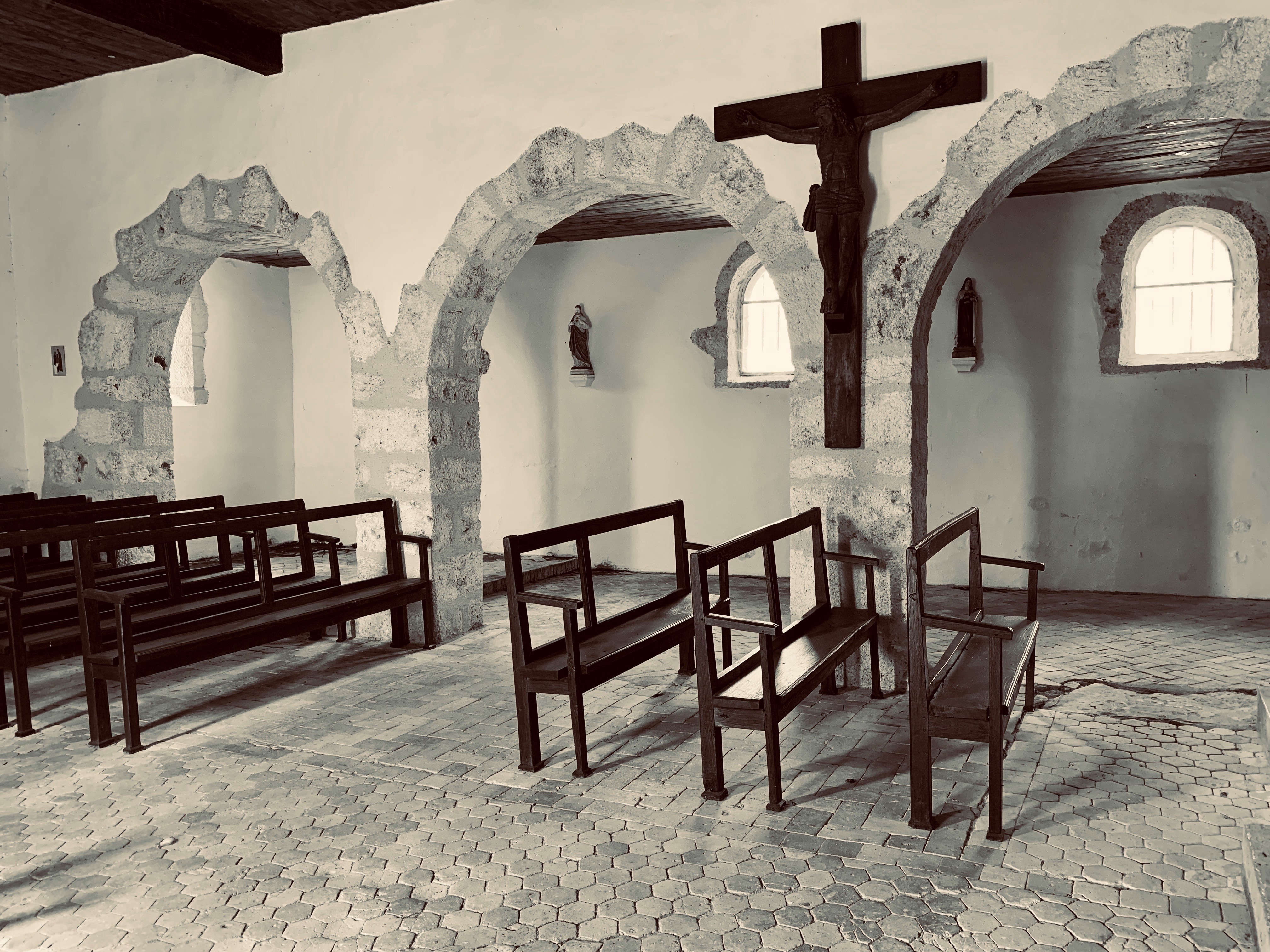 Intérieur de l'église Saint-Clément : arches romanes, crucifix et statues mariales