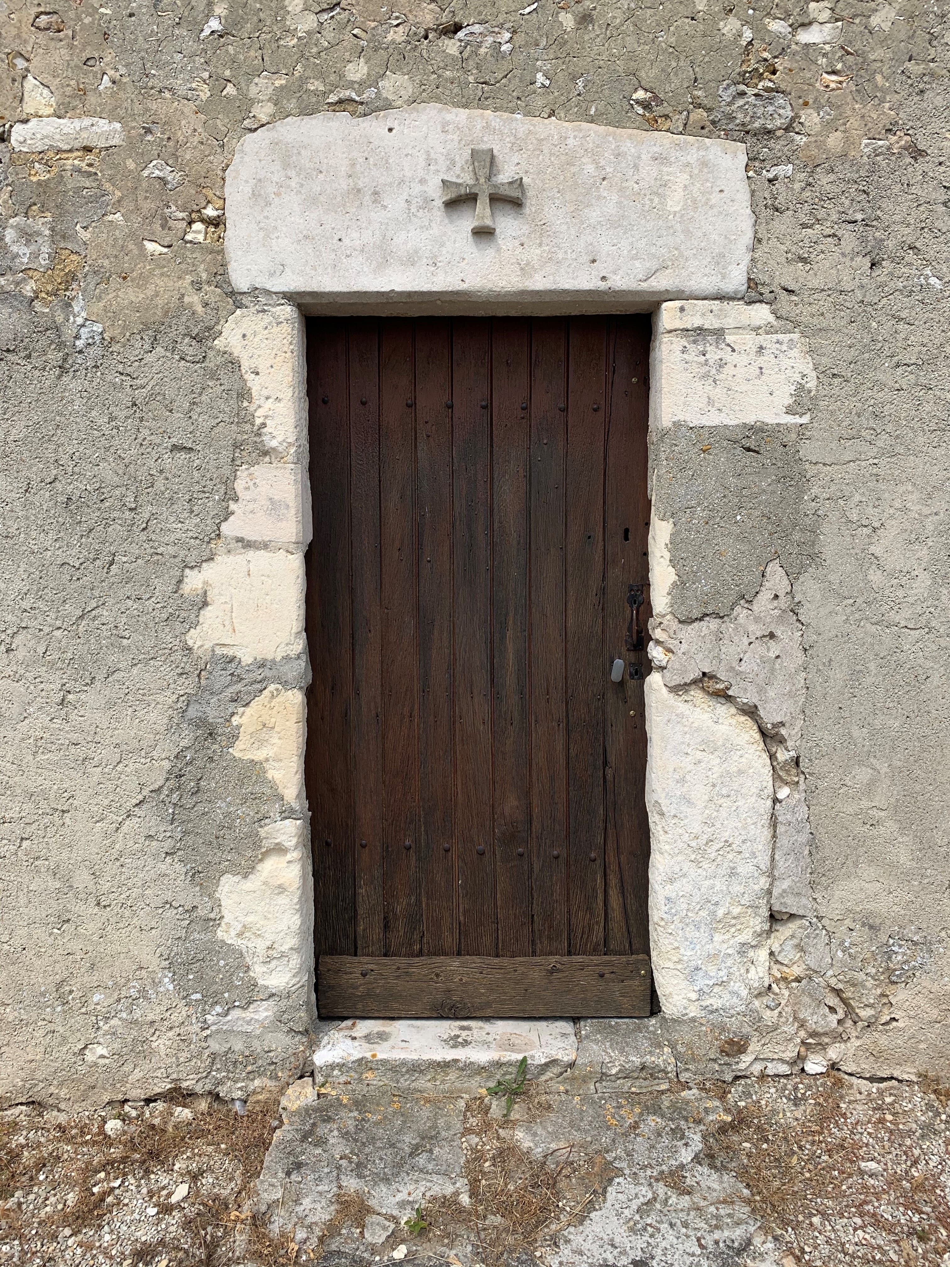 Porte latérale en bois sombre surmontée d'une croix templière sculptée